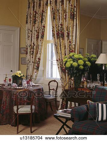 Red+cream patterned curtains in dining room with lime-green chrysanthemums in vase on table in front of mirror View Large Photo Image Picture - Red+cream patterned curtains in dining room with lime-green chrysanthemums in vase on table in front of mirror. Fotosearch