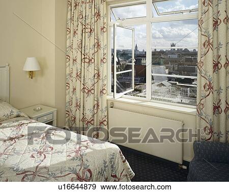 Stock Photo - Ribbon patterned curtains and matching bedcover in bedroom with cream radiator below window. Fotosearch