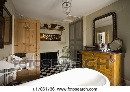 Roll-top bath in traditional bathroom with black+white chequerboard floor and pine chest-of-drawers View Large Photo Image Stock Photograph - Roll-top bath in traditional bathroom with black+white chequerboard floor and pine chest-of-drawers. Fotosearch
