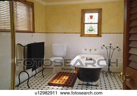 Stock Image - Rolltop bath and black+white chequerboard tiled floor in yellow and white bathroom. Fotosearch