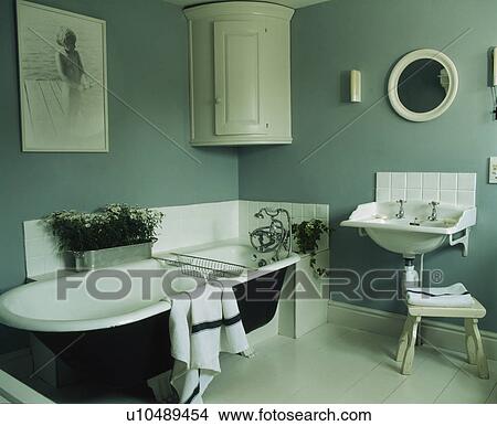 Picture - Rolltop bath and white corner cupboard in grey-blue bathroom. Fotosearch