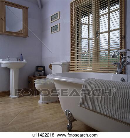Stock Photo - Rolltop bath in white bathroom with wooden flooring and slatted blind. Fotosearch