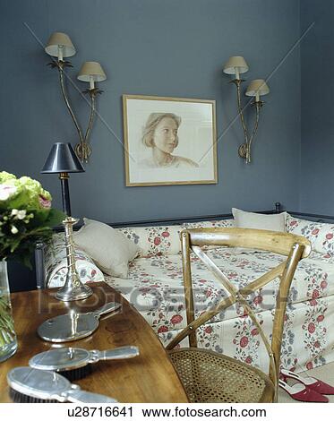 Stock Image - Silver dressing-table set on table with antique chair in small blue bedroom with floral sofa-bed. Fotosearch