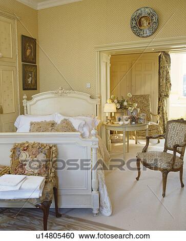 Stock Image - Single white bed and upholstered chair in comfortable country bedroom. Fotosearch