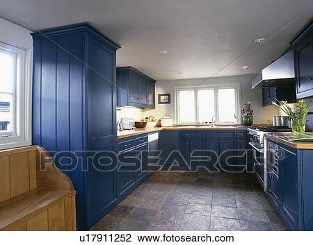 Stock Image - Slate tiled floor in country kitchen with fitted blue cupboards. Fotosearch