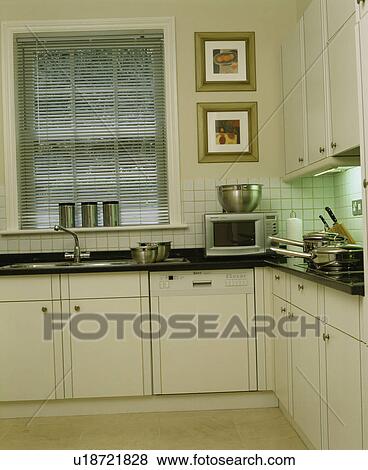 Stock Photo - Slatted blind on window in modern white townhouse kitchen. Fotosearch