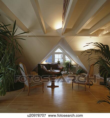 Small antique table and chairs in modern loft living room with tall houseplants and wooden flooring and triangular window View Large Photo Image Stock Photo - Small antique table and chairs in modern loft living room with tall houseplants and wooden flooring and triangular window. Fotosearch