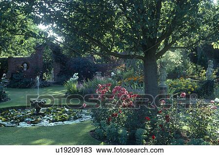 Stock Image - Small fountain in circular pool in country garden shaded by trees. Fotosearch