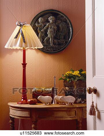 Stock Image - Small plaque on wallo above table with lighted lamp. Fotosearch