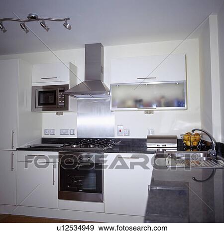 Stainless-steel extractor above oven and hob in small modern white kitchen with black granite worktops View Large Photo Image Stock Photo - Stainless-steel extractor above oven and hob in small modern white kitchen with black granite worktops. Fotosearch