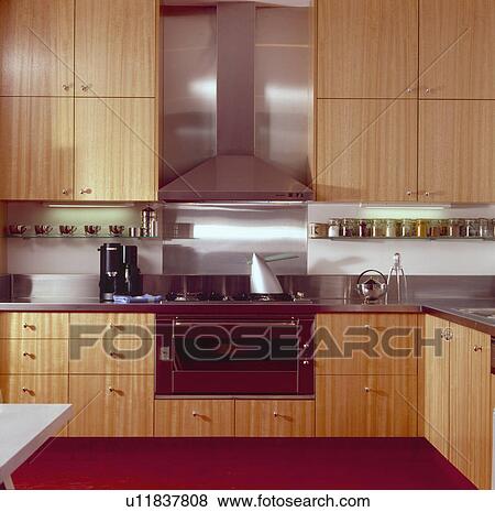 Stainless steel extractor and splashback above fitted oven in modern kitchen with pale wood fitted units View Large Photo Image Stock Photo - Stainless steel extractor and splashback above fitted oven in modern kitchen with pale wood fitted units. Fotosearch