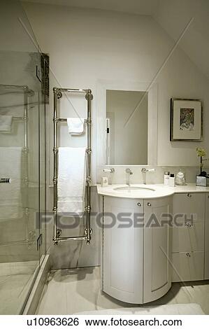Stainless steel heated towel rail in small cream bathroom with barrel-shaped doors on vanity unit View Large Photo Image Stock Photograph - Stainless steel heated towel rail in small cream bathroom with barrel-shaped doors on vanity unit. Fotosearch