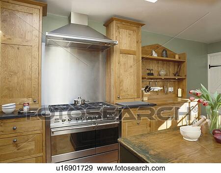 Stock Photo - Stainless-steel range oven in fitted wooden units in grey country kitchen. Fotosearch