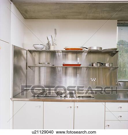 Stock Image - Stainless steel splashback and worktop in modern white kitchen. Fotosearch