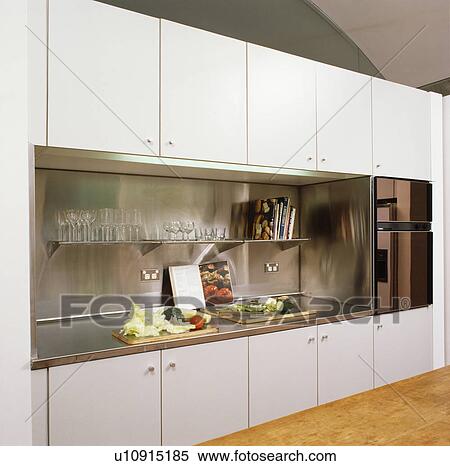 Stock Photography - Stainless steel splashback and worktops in modern white kitchen. Fotosearch