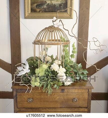 Stock Image - Still-Life of foliage and white flowers in informal flower arrangement on table with gilt birdcage. Fotosearch