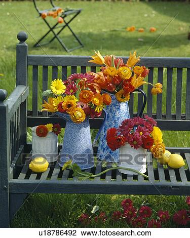 Still-Life of orange and yellow summer flowers in pale blue enamel jugs on wooden garden bench View Large Photo Image Stock Image - Still-Life of orange and yellow summer flowers in pale blue enamel jugs on wooden garden bench. Fotosearch