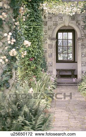 Stock Image - Stone path leading to stone seat in alcove in stone wall of country garden. Fotosearch