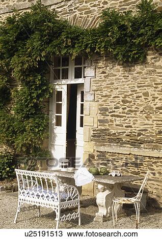 Stone table and white wrought-iron seat on patio outside doors of traditional stone house View Large Photo Image Stock Image - Stone table and white wrought-iron seat on patio outside doors of traditional stone house. Fotosearch
