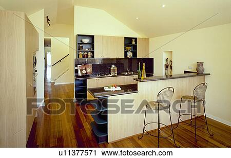 Stools at breakfast bar in modern cream kitchen with wooden flooring and pale wood units View Large Photo Image Stock Image - Stools at breakfast bar in modern cream kitchen with wooden flooring and pale wood units. Fotosearch