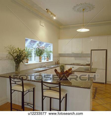 Stools at breakfast bar in modern white kitchen with black granite worktops on fitted units View Large Photo Image Stock Photo - Stools at breakfast bar in modern white kitchen with black granite worktops on fitted units. Fotosearch