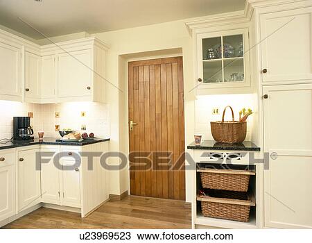Stock Image - Storage baskets in fitted unit beside wooden door in country kitchen. Fotosearch