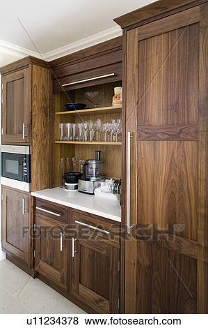 Storage shelves above appliances on white granite worktop in modern walnut kitchen View Large Photo Image Stock Photo - Storage shelves above appliances on white granite worktop in modern walnut kitchen. Fotosearch