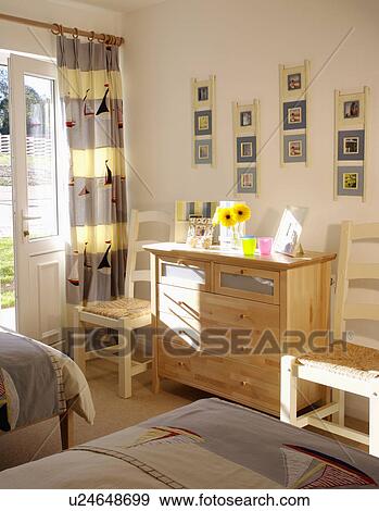 Striped boat motif curtains in modern bedroom with group of small pictures above chest of drawers View Large Photo Image Stock Photo - Striped boat motif curtains in modern bedroom with group of small pictures above chest of drawers . Fotosearch