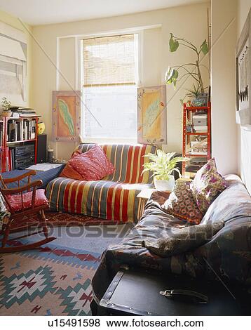 Striped throw on sofa below window with painted shutters in small living room View Large Photo Image Stock Photo - Striped throw on sofa below window with painted shutters in small living room. Fotosearch