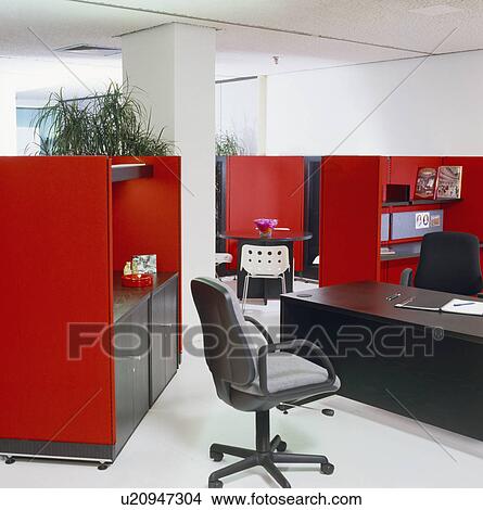 Swivel-chair and black desk in open-plan commercial office with red dividing cupboards View Large Photo Image Picture - Swivel-chair and black desk in open-plan commercial office with red dividing cupboards. Fotosearch