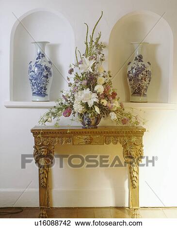Tall blue+white vases in arched alcoves on either side of formal floral arrangement on carved console table View Large Photo Image Stock Image - Tall blue+white vases in arched alcoves on either side of formal floral arrangement on carved console table. Fotosearch