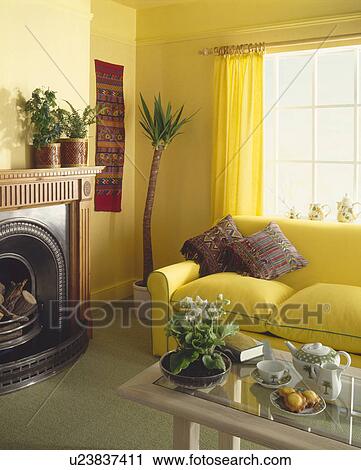 Stock Image - Teaset on glass coffee-table in yellow eighties living room with yellow sofa. Fotosearch