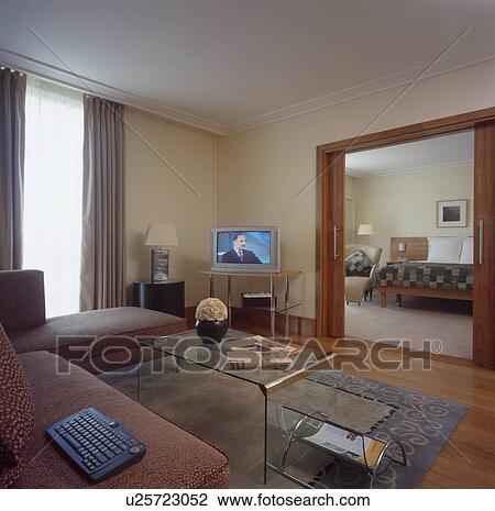 Stock Image - Television on in living room of hotel suite with door open to bedroom. Fotosearch