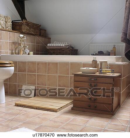 Terracotta tiled bath surround and floor in white attic bathroom with storage drawers View Large Photo Image Stock Image - Terracotta tiled bath surround and floor in white attic bathroom with storage drawers. Fotosearch