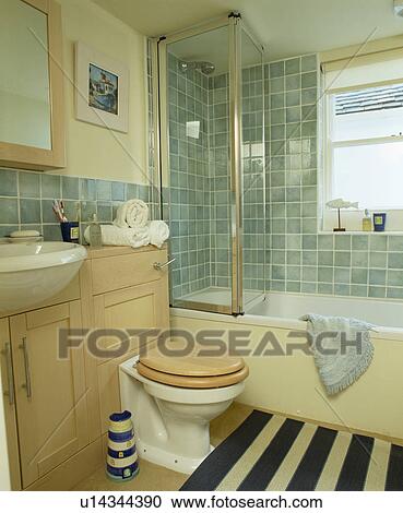 Stock Image - Toilet beside bath with glass shower door in turquoise tiled bathroom. Fotosearch