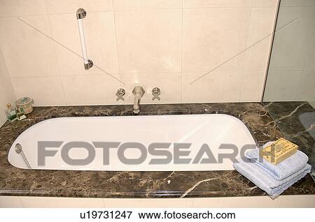 Stock Photo - Towels on side of bath with marble surround in modern bathroom. Fotosearch