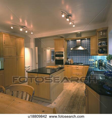 Stock Image - Track lighting in modern kitchen with granite-topped island unit and reclaimed floorboards. Fotosearch