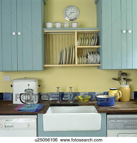 Stock Photograph - Turquoise fitted cupboards and plate rack above Belfast sink. Fotosearch