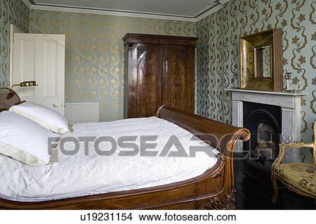 Picture - Turquoise+gold Osborne+Little wallpaper in traditional bedroom with oak antique lit bateau bed. Fotosearch