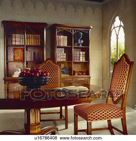 Stock Photo - Upholstered Gothic-style chair and circular antique table in small hotel library. Fotosearch