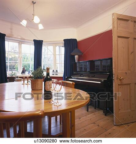 Stock Image - Varnished pine table in red dining room with piano. Fotosearch
