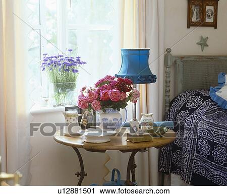 Vase of pink roses with blue lamp on circular bedside table View Large Photo Image Stock Image - Vase of pink roses with blue lamp on circular bedside table. Fotosearch