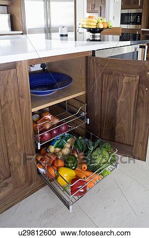 Stock Image - Vegetables stored in pull-out wire drawers in modern kitchen. Fotosearch