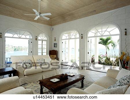 View of the sea through large arched French doors in Caribbean living room cream sofas and wooden ceiling View Large Photo Image Stock Image - View of the sea through large arched French doors in Caribbean living room cream sofas and wooden ceiling. Fotosearch