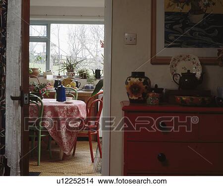 Picture - View through open doorway of red chair and patterned red cloth on table in small dining room. Fotosearch
