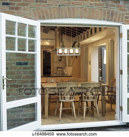 View through open French windows of dining room extension with wooden chairs and table View Large Photo Image Stock Photo - View through open French windows of dining room extension with wooden chairs and table. Fotosearch