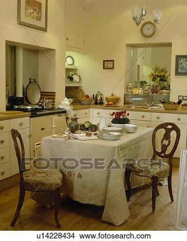 Picture - Vintage linen cloth on table with upholstered Victorian chairs in cream country kitchen. Fotosearch