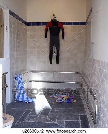 Stock Image - Wetsuit hanging up to dry in modern tiled bathroom with slate flooring. Fotosearch
