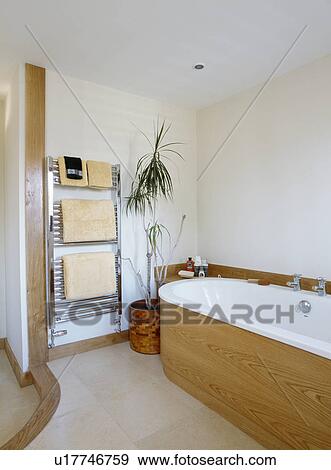White bath with pale wood panelling in modern white bathroom with stainless steel heated towel rail View Large Photo Image Stock Photo - White bath with pale wood panelling in modern white bathroom with stainless steel heated towel rail. Fotosearch