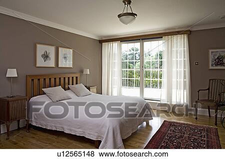 White bed linen in modern beige bedroom with white voile curtains at French windows View Large Photo Image Stock Photo - White bed linen in modern beige bedroom with white voile curtains at French windows. Fotosearch